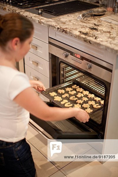 Teenagermädchen stellt Backblech mit Keksen in den Ofen