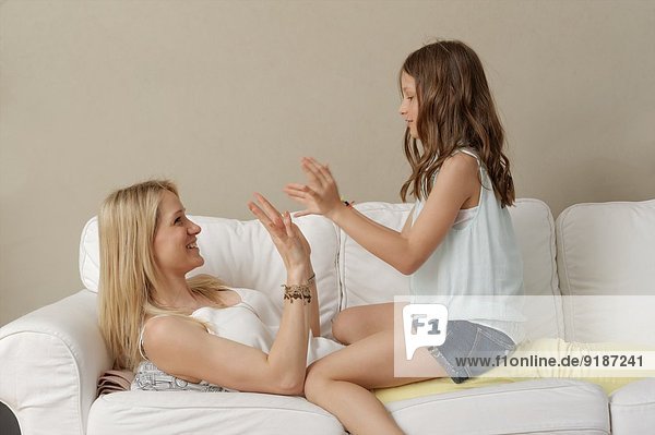 Mutter und Tochter beim Händeklatschen auf dem Sofa