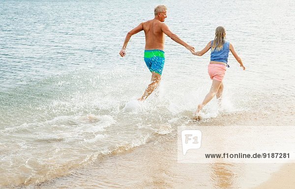 Vater und Tochter rennen und Händchen halten am Strand