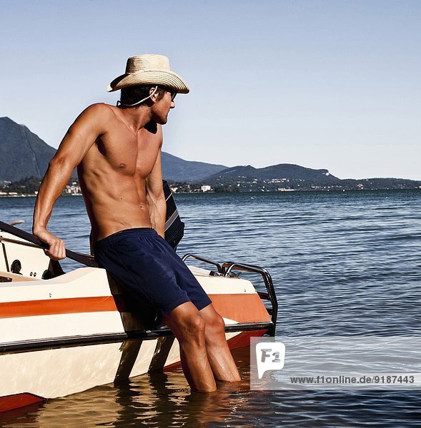 Junger Mann,  der sich gegen ein Motorboot lehnt,  Verbania,  Italien