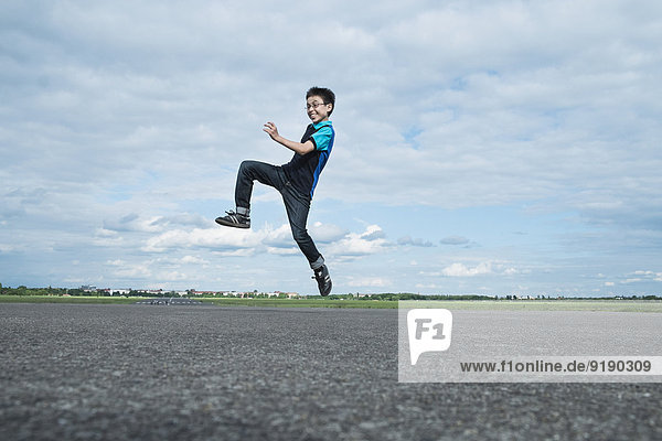 Full length excited boy jumping on road against cloudy sky