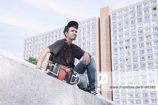 Nachdenklicher junger Mann mit Skateboard  der gegen den Bau sitzt.
