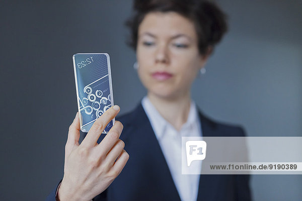 Nahaufnahme einer Geschäftsfrau mit Blick auf ein transparentes Mobiltelefon