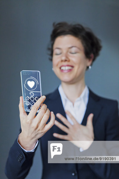 Glückliche Geschäftsfrau Holding Transparentes Smartphone mit Herzform
