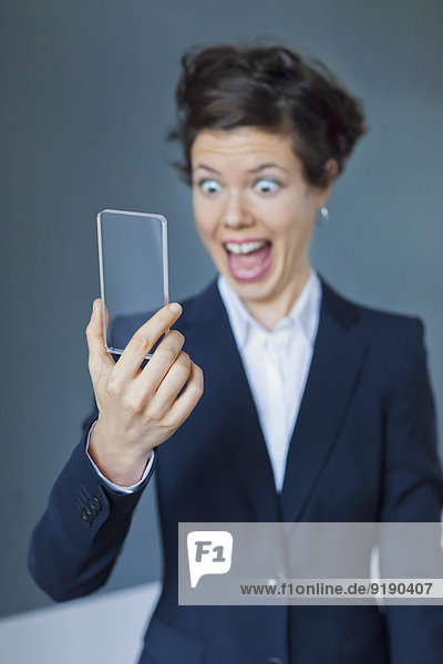 Ekstatische Geschäftsfrau schaut auf ein leeres  futuristisches  transparentes Smartphone.