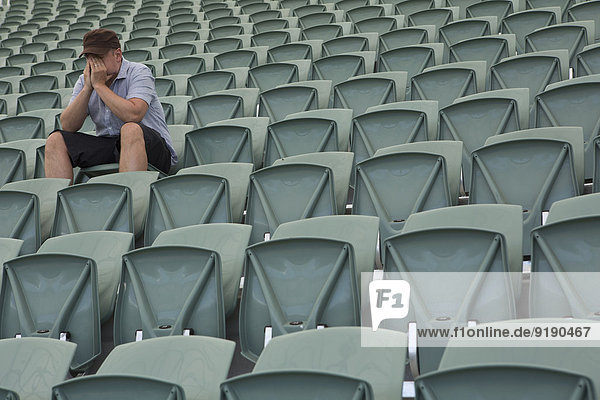 Trauriger Mann sitzt allein im leeren Stadion.