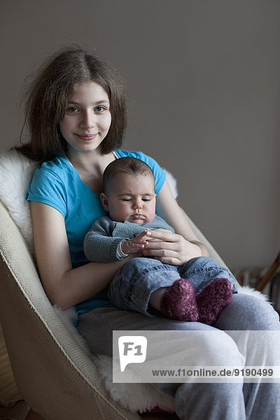 Porträt der lächelnden Schwester mit dem Mädchen auf dem Stuhl zu Hause