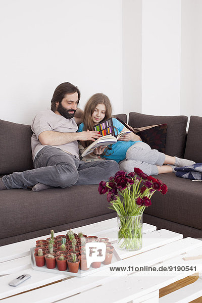 Vater und Tochter lesen gemeinsam im Wohnzimmer.