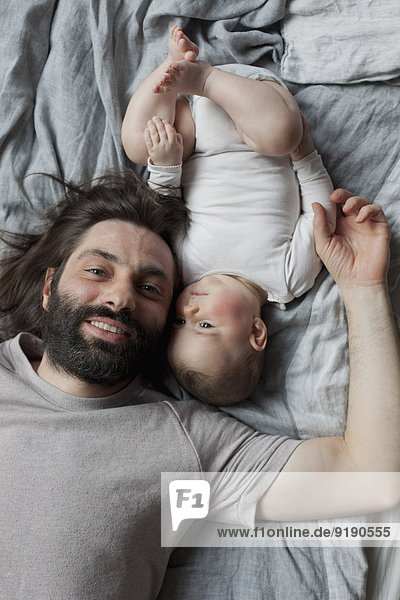 Porträt eines lächelnden Vaters mit im Bett liegendem Mädchen
