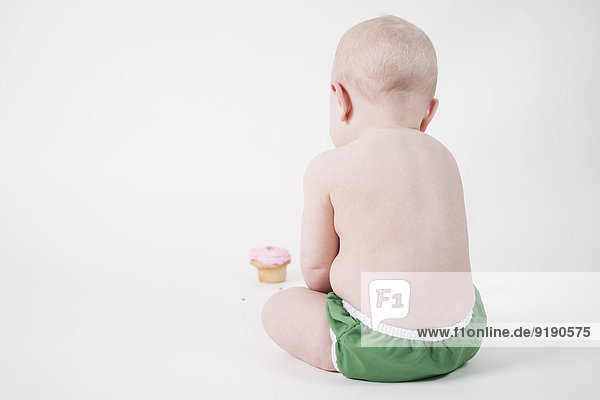 Rückansicht des Babys mit Blick auf Cupcake vor weißem Hintergrund
