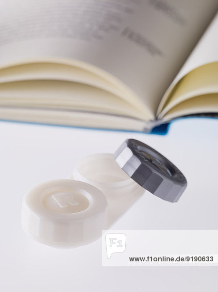 Nahaufnahme von Kontaktlinsenetui und Buch auf weißem Hintergrund