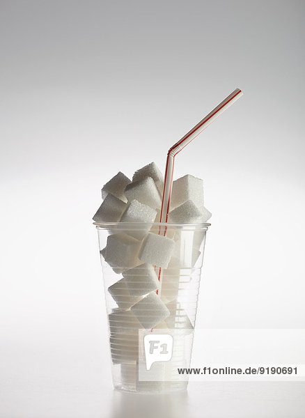 Stroh in Plastikglas gefüllt mit Zuckerwürfeln auf grauem Hintergrund