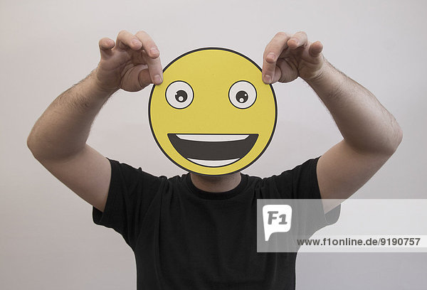 Mann mit einem wirklich glücklichen Emoticon-Gesicht vor dem Gesicht