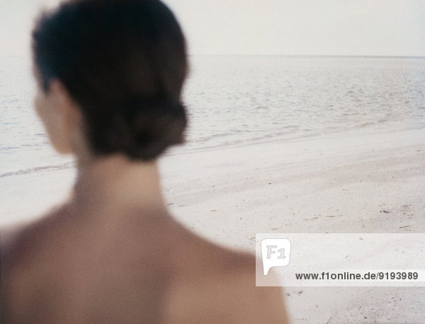 Frau mit Blick auf den Ozean  Rückansicht von Kopf und Schultern  Strandfokus im Hintergrund