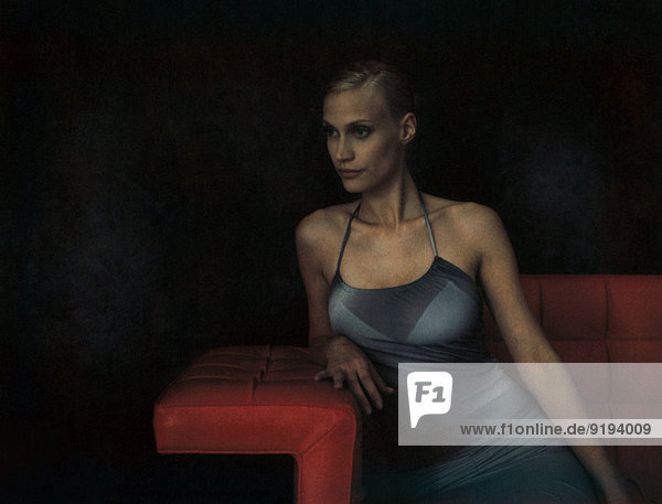 Elegante junge Frau auf dem Sofa sitzend  auf dem Ellenbogen lehnend  wegschauend
