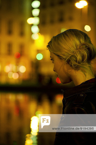 Junge Frau bei Nacht am Fluss  beleuchtet von Stadtlichtern