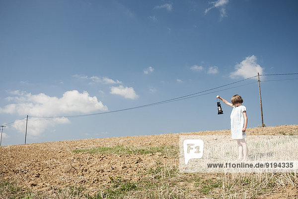 Mädchen im Feld stehend mit altmodischer Laterne,  Blick auf die Stromleitung