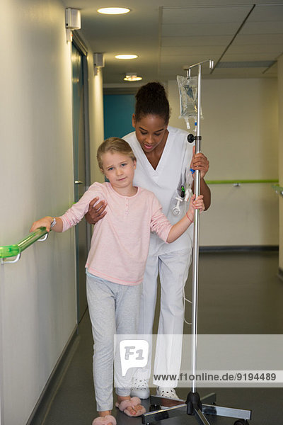 Female nurse helping to a girl patient to walk in hospital corridor