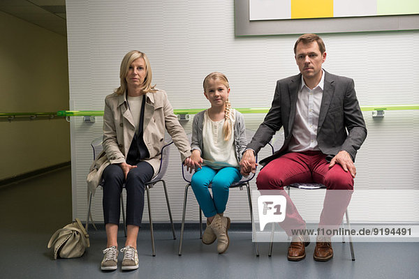 Couple with their daughter sitting in the waiting area of a hospital