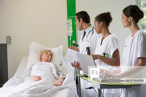Medical team discussing female patient record in hospital bed