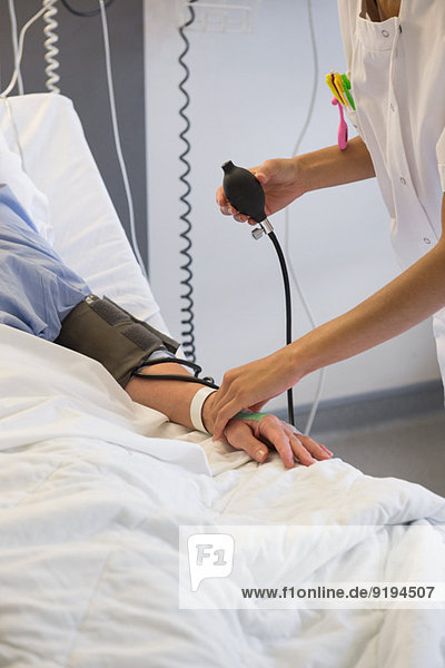 Krankenschwester  die den Blutdruck des Patienten auf dem Krankenhausbett kontrolliert.