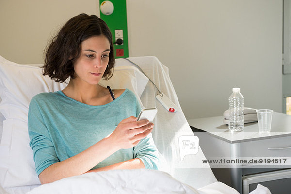 Female patient reclining on a hospital bed and text messaging