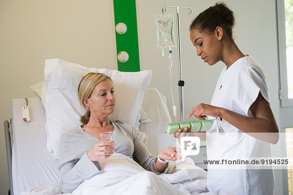 Female nurse discussing pill box with patient on hospital bed