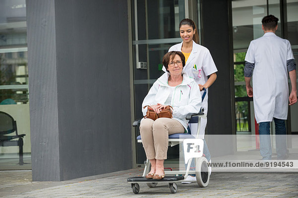 Ärztin schiebt eine Patientin  die auf einem Stuhl sitzt.