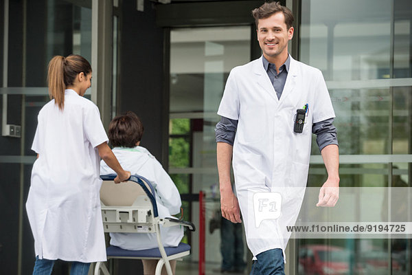 Male doctor smiling with a female doctor pushing a patient sitting in a chair