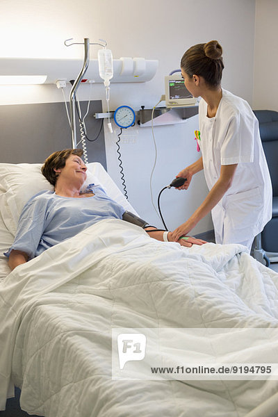 Female nurse checking patient's blood pressure on hospital bed
