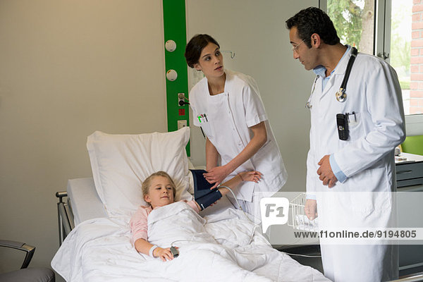 Medical attendants examining to a girl patient in hospital bed