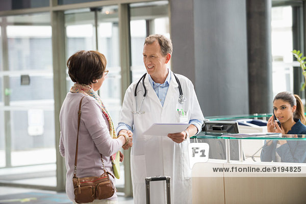 Male doctor shaking hands with his patient at hospital reception desk