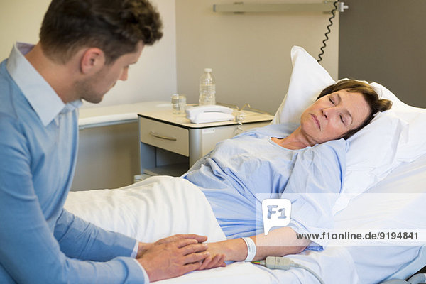 Mann hält Hände seiner Mutter im Krankenhausbett