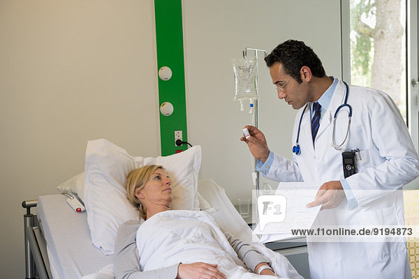 Male doctor giving pills instructions to female patient in hospital bed