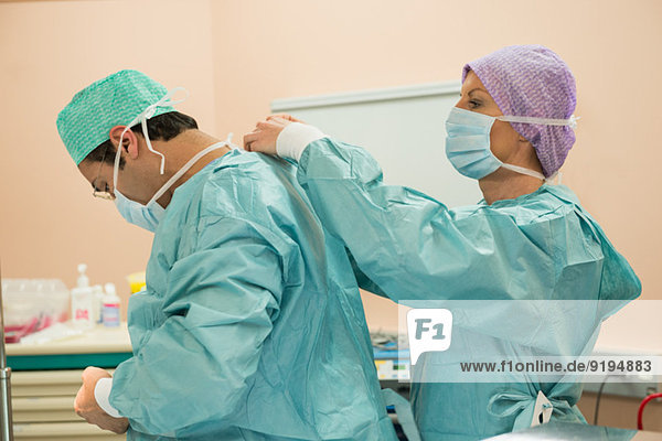 Chirurgin hilft einem Chirurgen beim Anziehen der Schutzkleidung