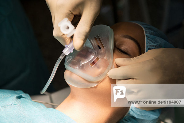 Anesthetist holding oxygen mask over patient's mouth in an operating room