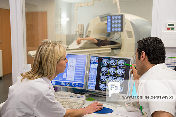 Ärzte untersuchen Scan am Computer mit Patient auf MRT-Scanner im Hintergrund