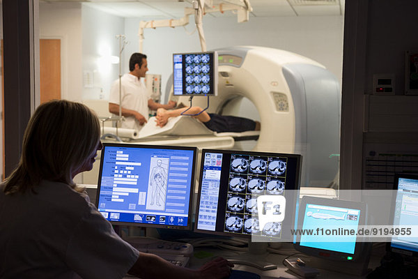 Ärztin untersucht Scan am Computer mit Patientin auf MRT-Scanner im Hintergrund