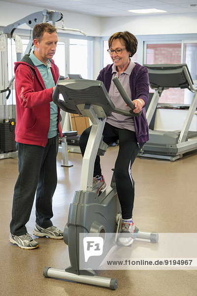 Trainer helping a woman with the cycle in a gym