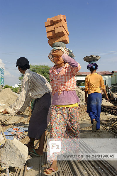 Bauarbeiterinnen tragen Backsteine auf dem Kopf auf einer Hochhausbaustelle Mandalay Myanmar