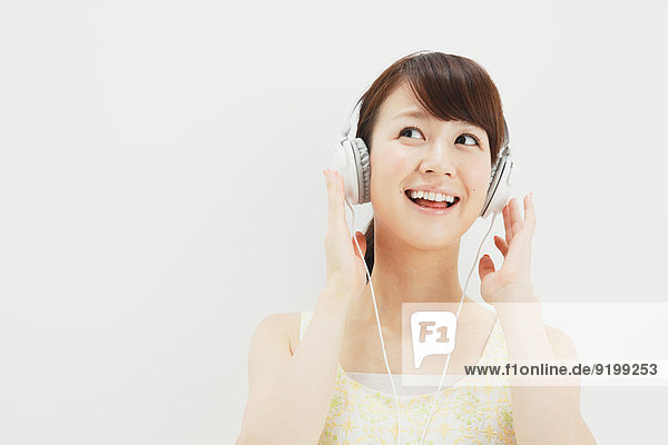 Japanese young woman in a one piece dress with earphones standing against white background