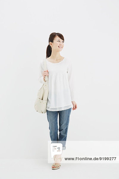 Japanese young woman in jeans and white shirt standing against white background