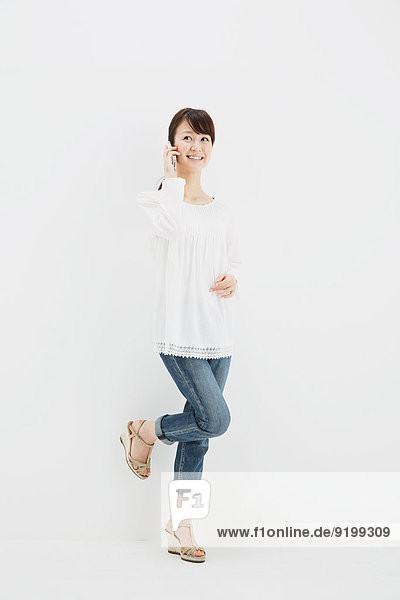 Japanese young woman in jeans and white shirt with smartphone standing against white background