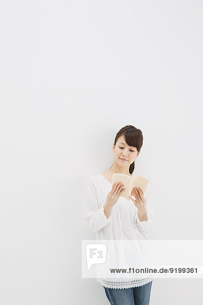 Japanese young woman in jeans and white shirt with a book against white background