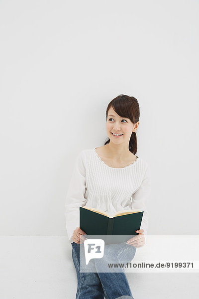 Japanese young woman in jeans and white shirt with a book against white background