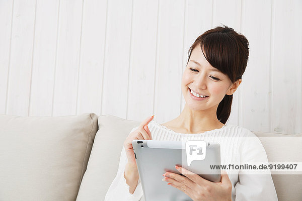 Japanese young woman in a white shirt with tablet on the sofa