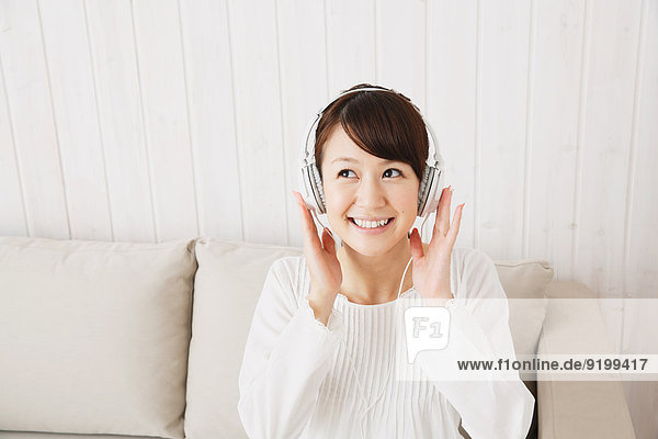 Japanese young woman in a white shirt with earphones on the sofa