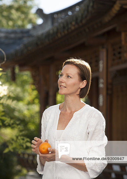 Frau steht vor Pagodenbau  Apfelsine in der Hand