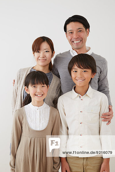 Young Japanese couple with two kids standing and smiling while cuddling