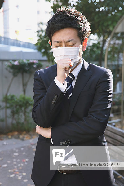 Sick Japanese young businessman in a suit at the park